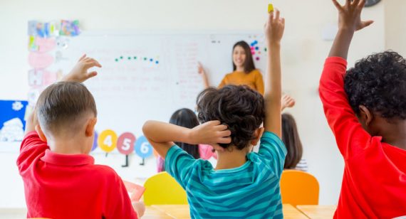 Preschool kid raise arm up to answer teacher question on whiteboard in classroom,Kindergarten education concept.